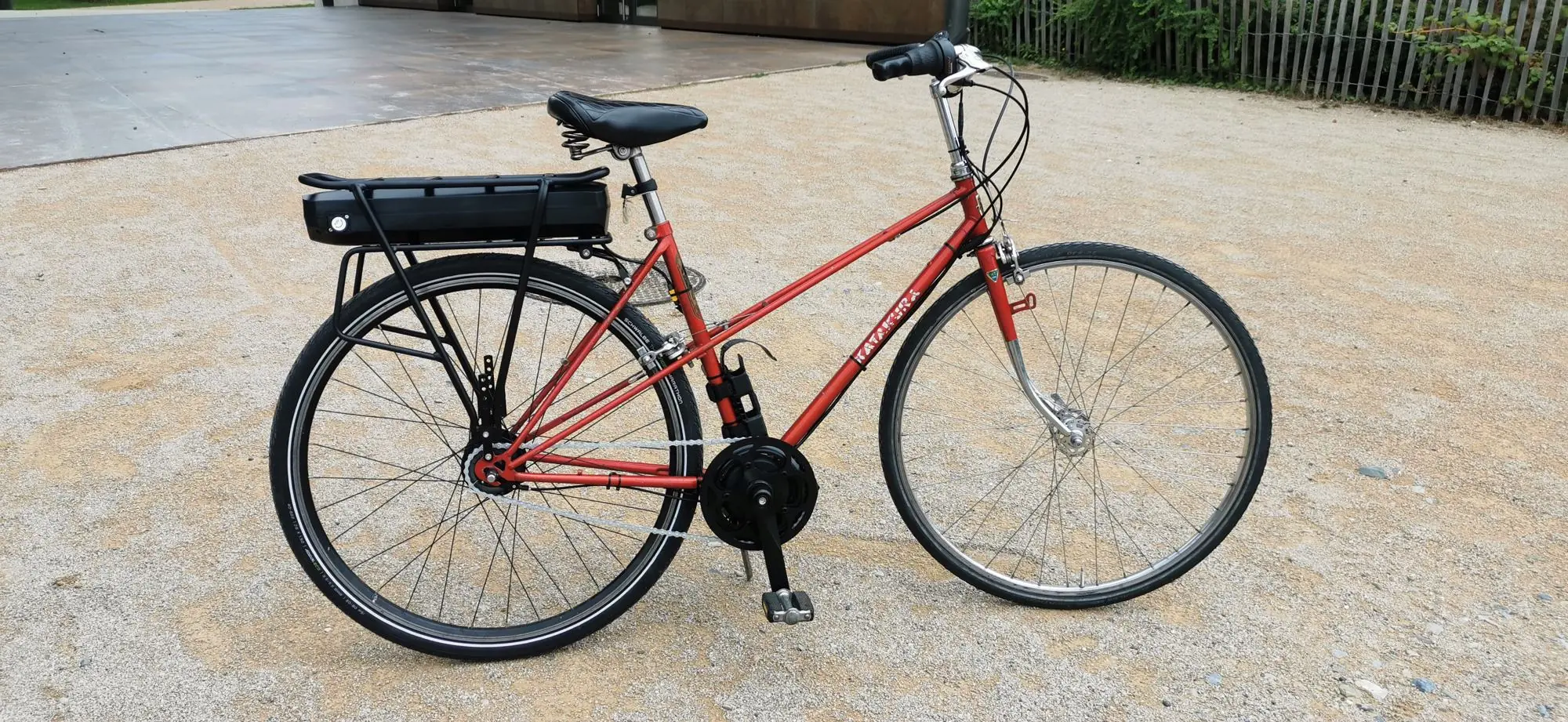 Vélo de ville rouge motorisé, avec sa batterie sur le porte-bagage arrière
