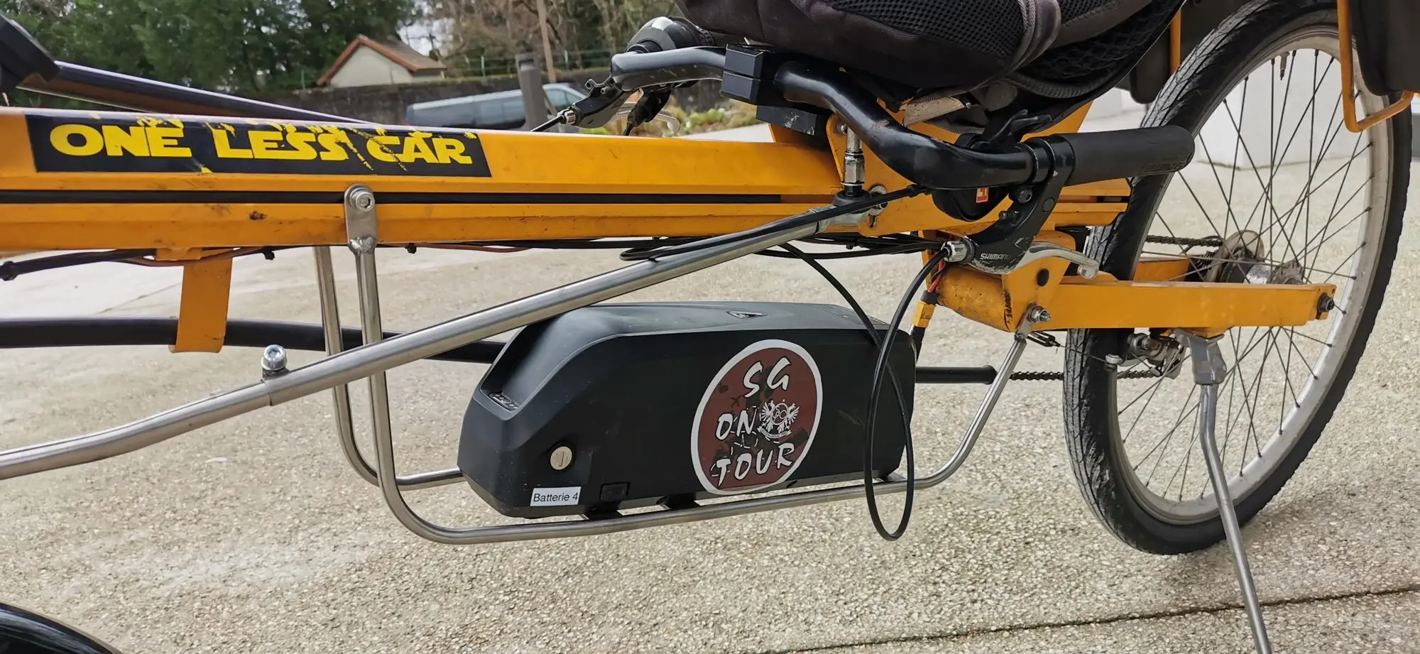 Batterie noire suspendue dans un porte-bagage en Inox sous le cadre d’un vélo couché jaune